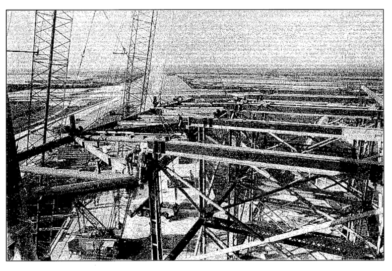 Small-format photograph: Wilhoit Steel Erectors has lifted the RSS Bottom Truss Weldment almost the full eighty some-odd vertical feet it needs to travel, to permit it to then be moved out and across the top of the Falsework which you see clearly in this image, taken from the FSS at Elevation 140. The Union Ironworkers who were visible on the Falsework in the larger color image above this one have all moved out to positions on top of the suspended Truss, and will be working the rigging for the next phase of this lift.